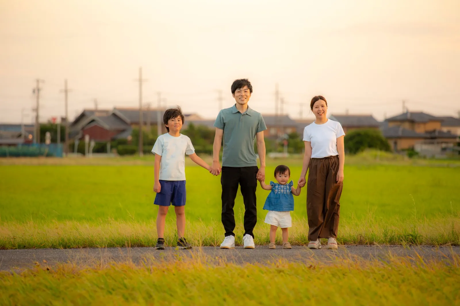 夕方の田んぼ道で手をつなぐ家族